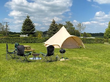 Six-metre bell tent with picnic bench, barbecue and camp chairs around the firepit